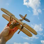 Wooden biplane model held in hand against sky