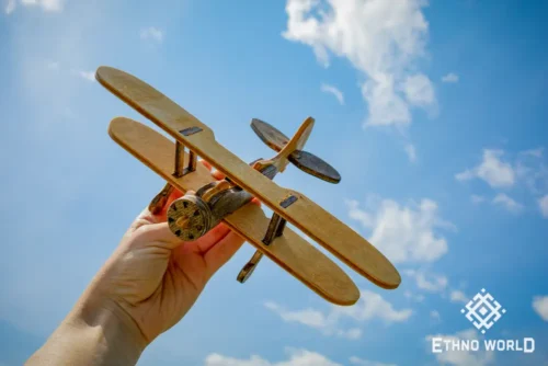 Wooden biplane model held in hand against sky