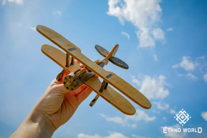 Wooden biplane model held in hand against sky